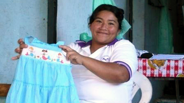 Stickerin aus El-Salvador hält stolz ein selbst besticktes Kleid in die Kamera.