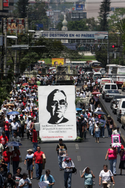 Plakat bei der Demo in El Salvador zum 30. Todestag von Oscar Romero inmitten eines Straßenzugs