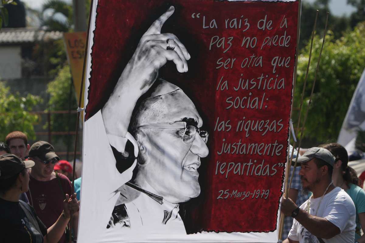 Plakat bei der Demo in El Salvador zum 30. Todestag von Oscar Romero inmitten eines Straßenzugs