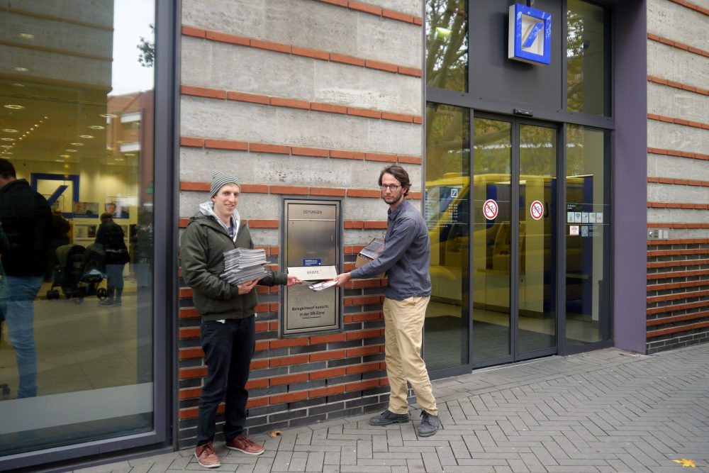 CIR-Referenten Christian Wimberger und Patrick Niemann mit den gesammelten Protespostkarten vor einer Filiale der Deutschen Bank