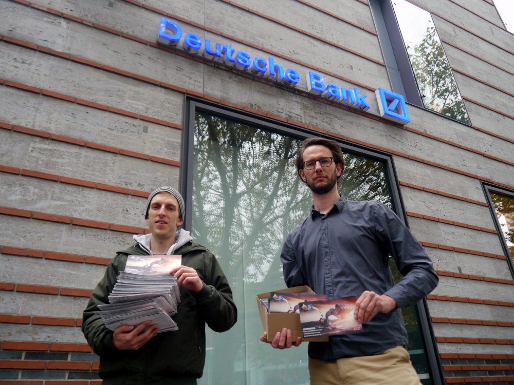 CIR-Referenten Christian Wimberger und Patrick Niemann mit den gesammelten Protespostkarten vor einer Filiale der Deutschen Bank