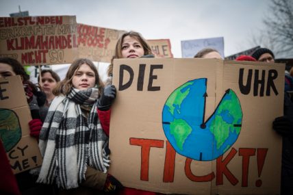 Mehrere FridaysForFuture Demonstrant*innen halten Plakate, unter anderem eines mit einer Weltkugel als Uhr und dem Schriftzug "Die Uhr tickt"