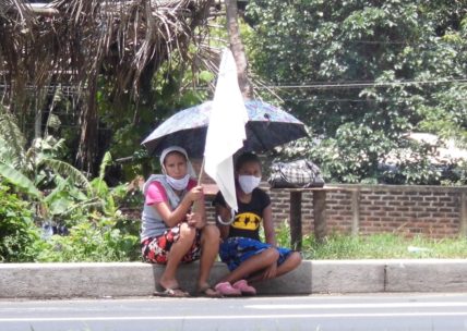 Zwei Menschen sitzen in El Salvador mit einer weißen Fahne in der Hand am Straßenrand