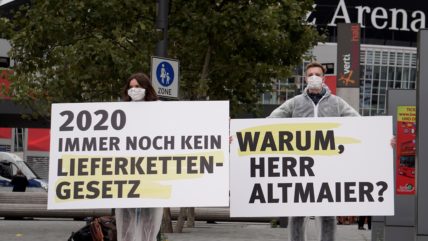 Aktivist*innen der Initiative Lieferkettengesetz protestieren beim Tag der Deutschen Industrie mit Plaketen.