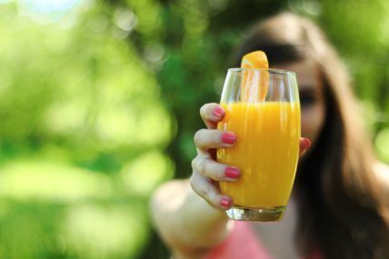 Frau hält Glas mit Orangensaft in Kamera