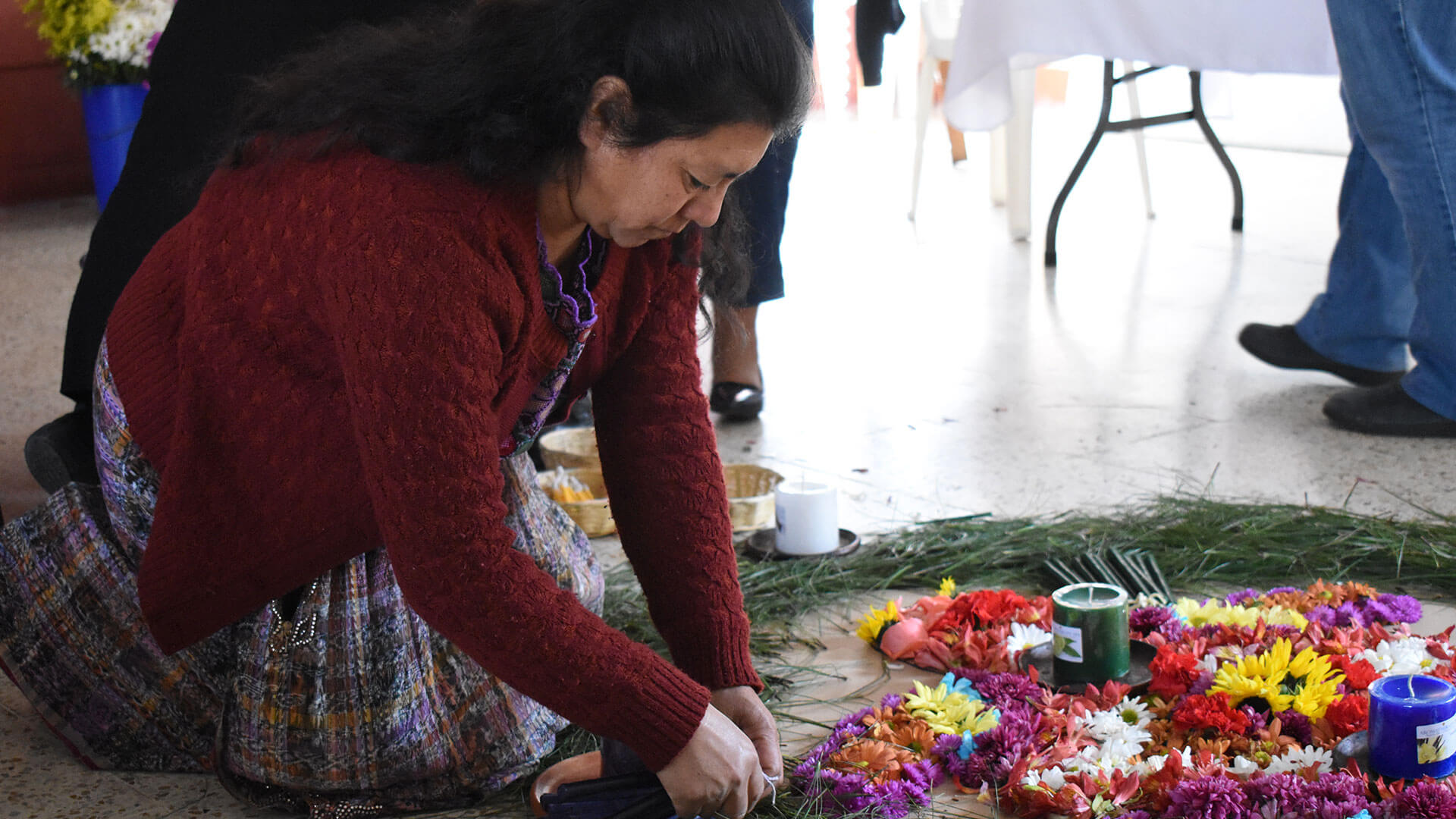 Eine Person legt Blumenkränze und Kerzen auf den Boden, sie kniet dabei.
