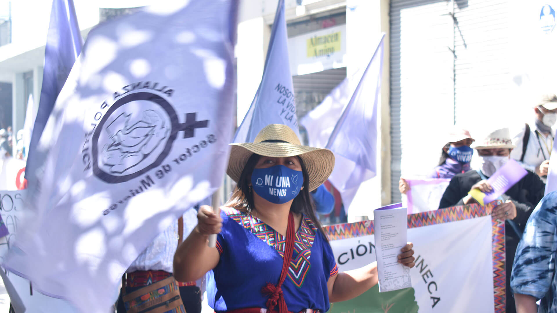 Demonstrierende mit Maske mit der Aufschrift "Ni una menos". Außerdem eine lila Fahne.